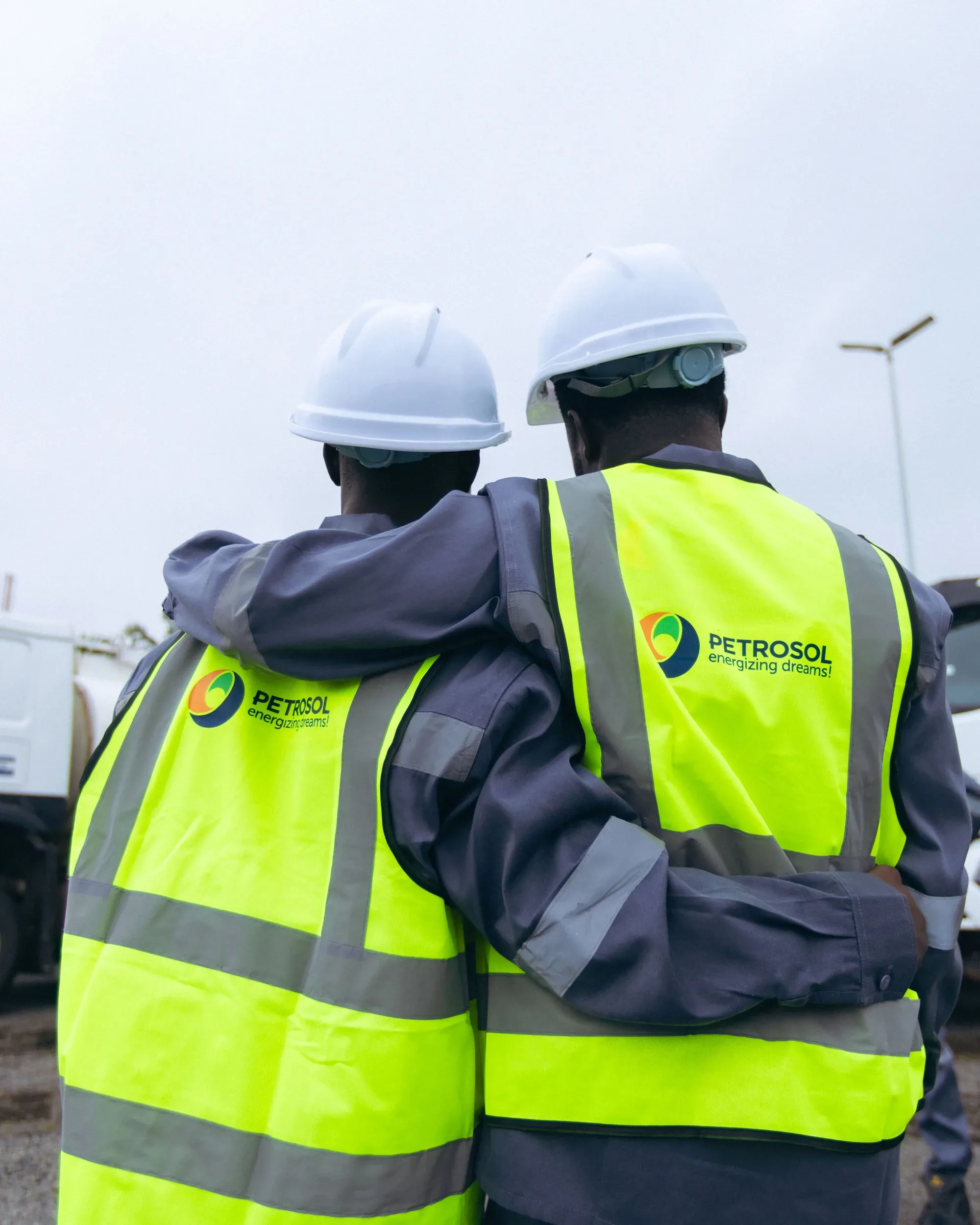 Two PETROSOL workers in hard hats and branded high-visibility vests standing arm in arm