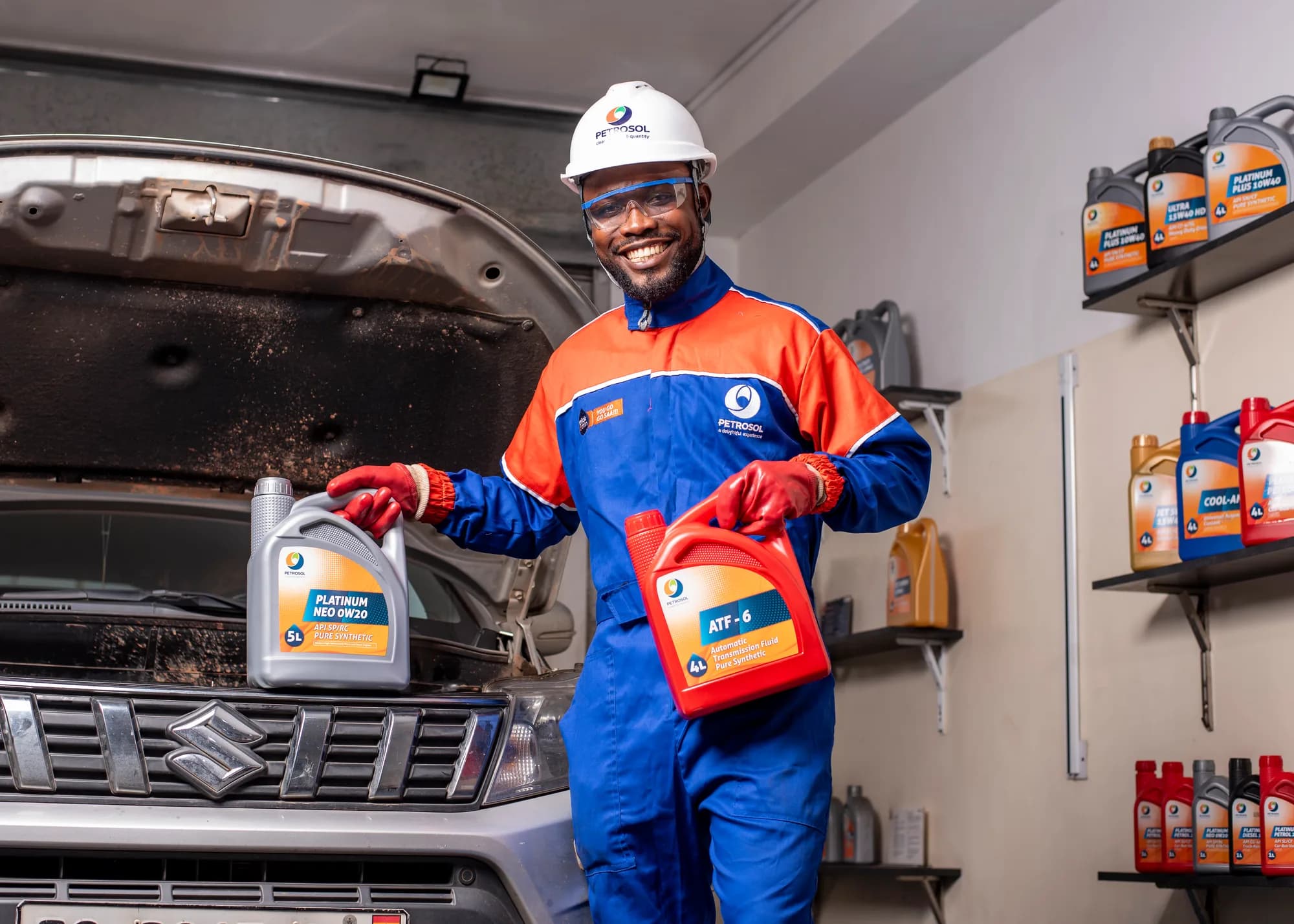 A PETROSOL technician in the lube bay holding Platinum NEO 0W20 and ATF-6, with the Platinum range on the shelves behind